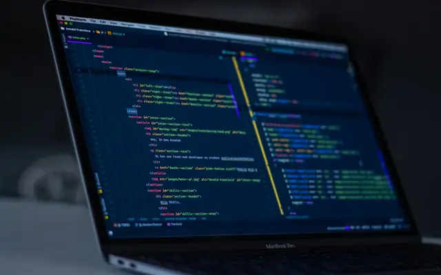 Laptop on a desk showing website code in a dark editor